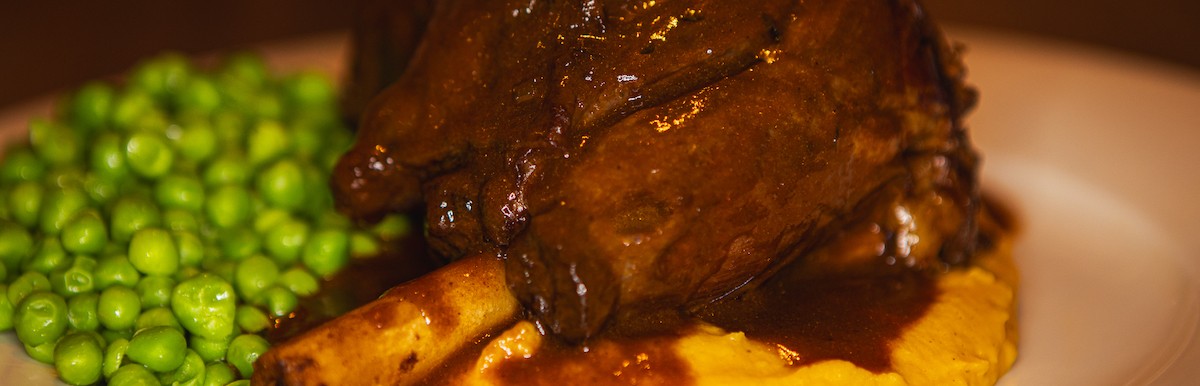 Langzaam gegaarde Lamsschenkel met zoete aardappelpuree en doperwtjes 